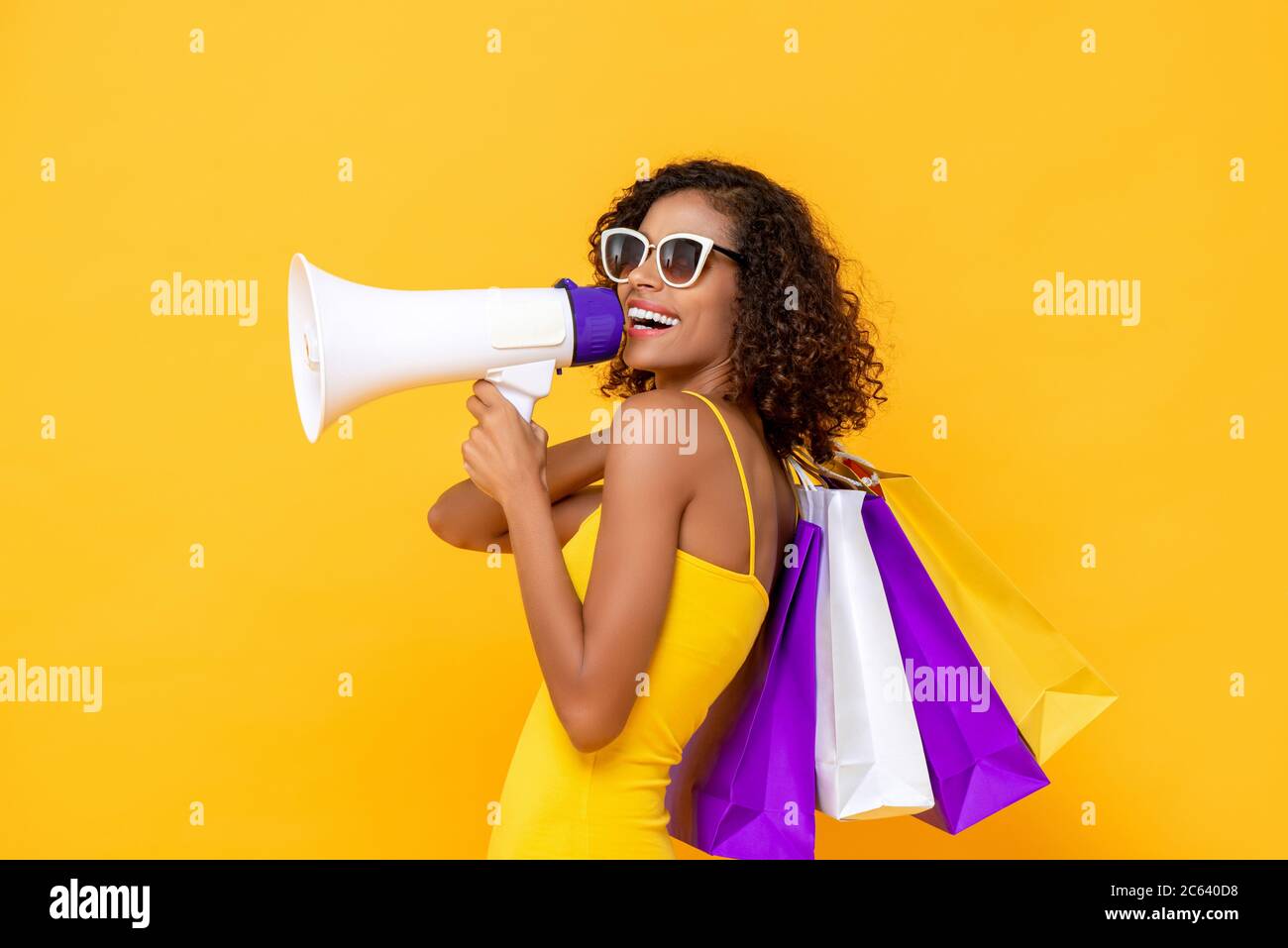 Felice bella donna con borse e megafono shopping su isolato sfondo giallo colorato per la vendita e concetti di sconto Foto Stock