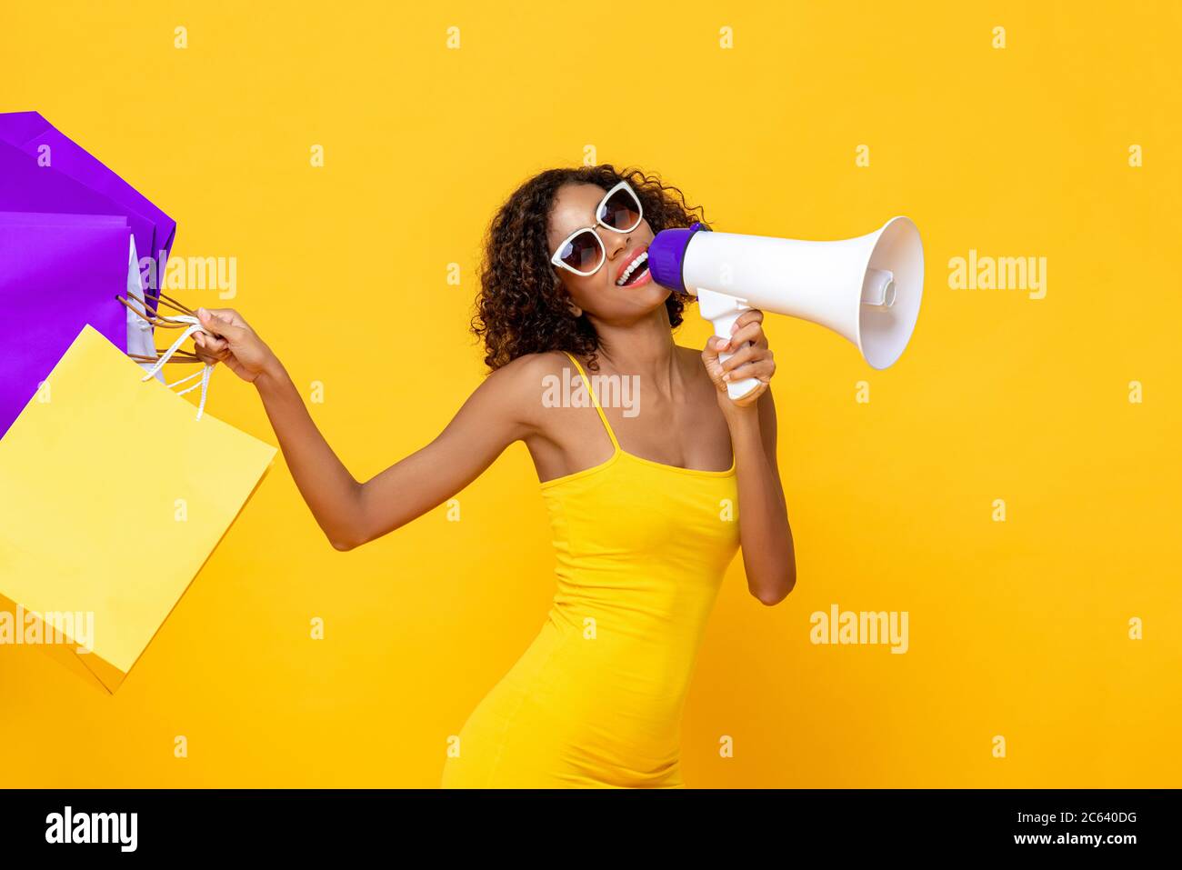 Felice bella donna con borse e megafono shopping su isolato sfondo giallo colorato per la vendita e concetti di sconto Foto Stock