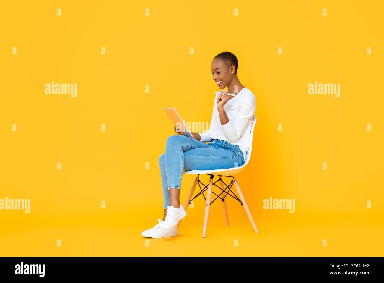 Giovane donna afroamericana seduto e utilizzando un computer tablet con penna stilo su sfondo giallo isolato Foto Stock