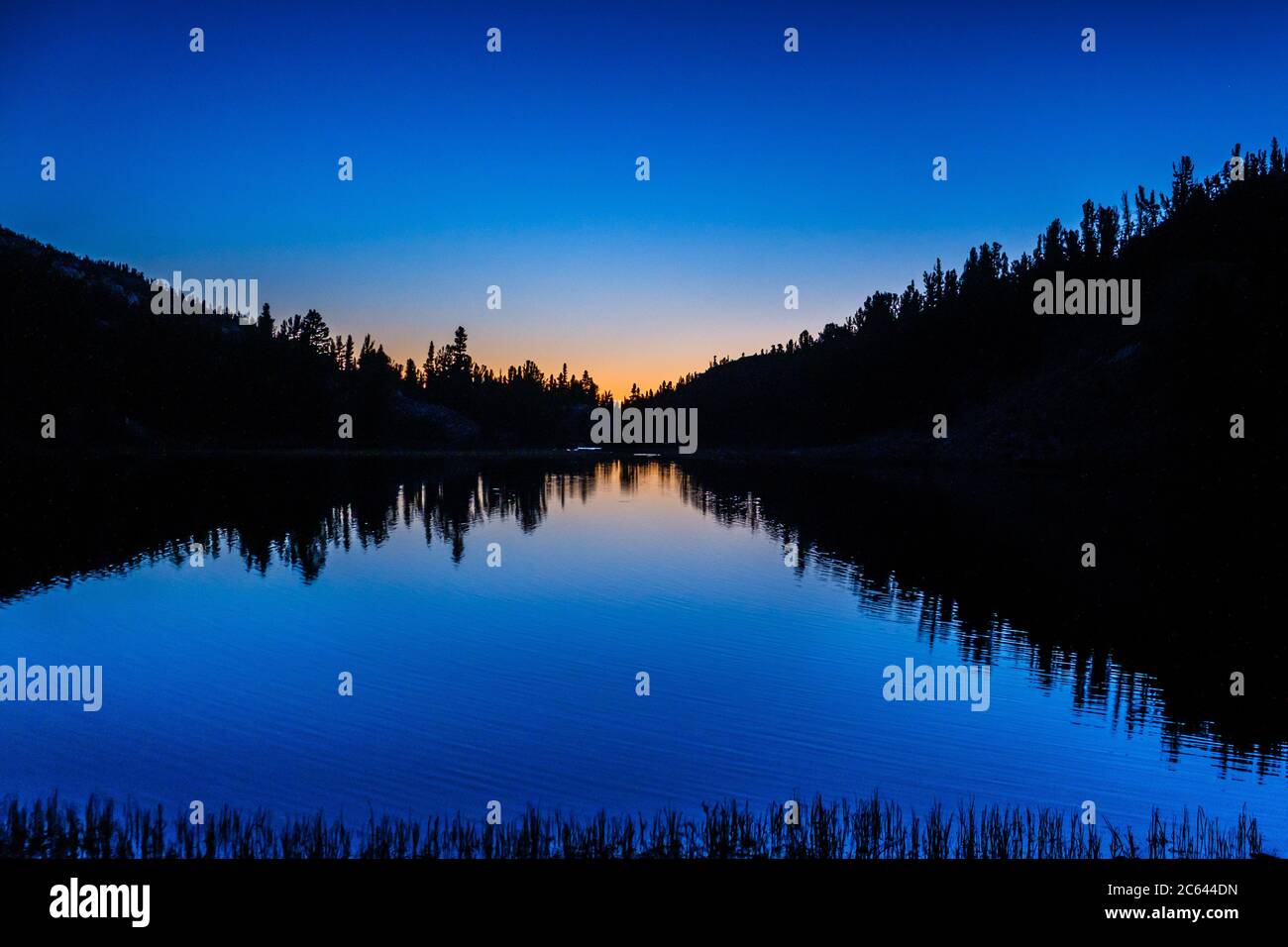 Una silhouette del paesaggio come la prima luce infrange l'orizzonte in un lago di montagna Foto Stock