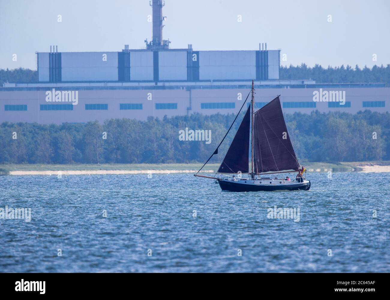 Lubmin, Germania. 02 luglio 2020. Una barca a vela sta navigando sul Greifswalder Bodden di fronte alla ex sede DI 'VE Kombinat Kernkraftwerke Bruno Leuschner'. Quando la centrale elettrica fu chiusa nel 1990 e i lavori di costruzione degli ultimi due blocchi furono interrotti, anche il complesso edilizio lungo 126 metri e alto 50 metri divenne un orfano. Il cumulo nucleare di Lubmin era destinato a rendere la RDT autosufficiente nelle importazioni di elettricità. Credit: Jens Büttner/dpa-Zentralbild/ZB/dpa/Alamy Live News Foto Stock