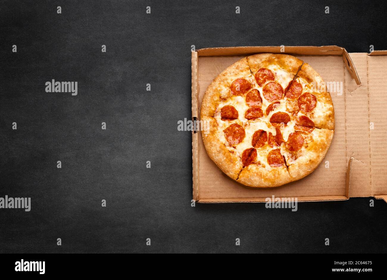 Pizza in una scatola di cartone su una lavagna scura. Spazio per il testo. Vista dall'alto del pacchetto pizza. Consegna pizza. Foto Stock