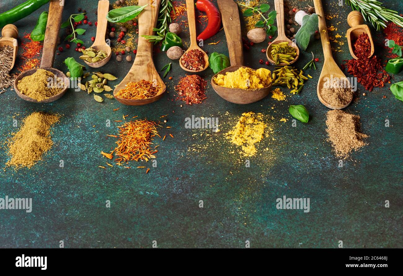 Varie spezie ed erbe secche su sfondo verde scuro. Vista dall'alto delle spezie in cucchiai di legno Foto Stock