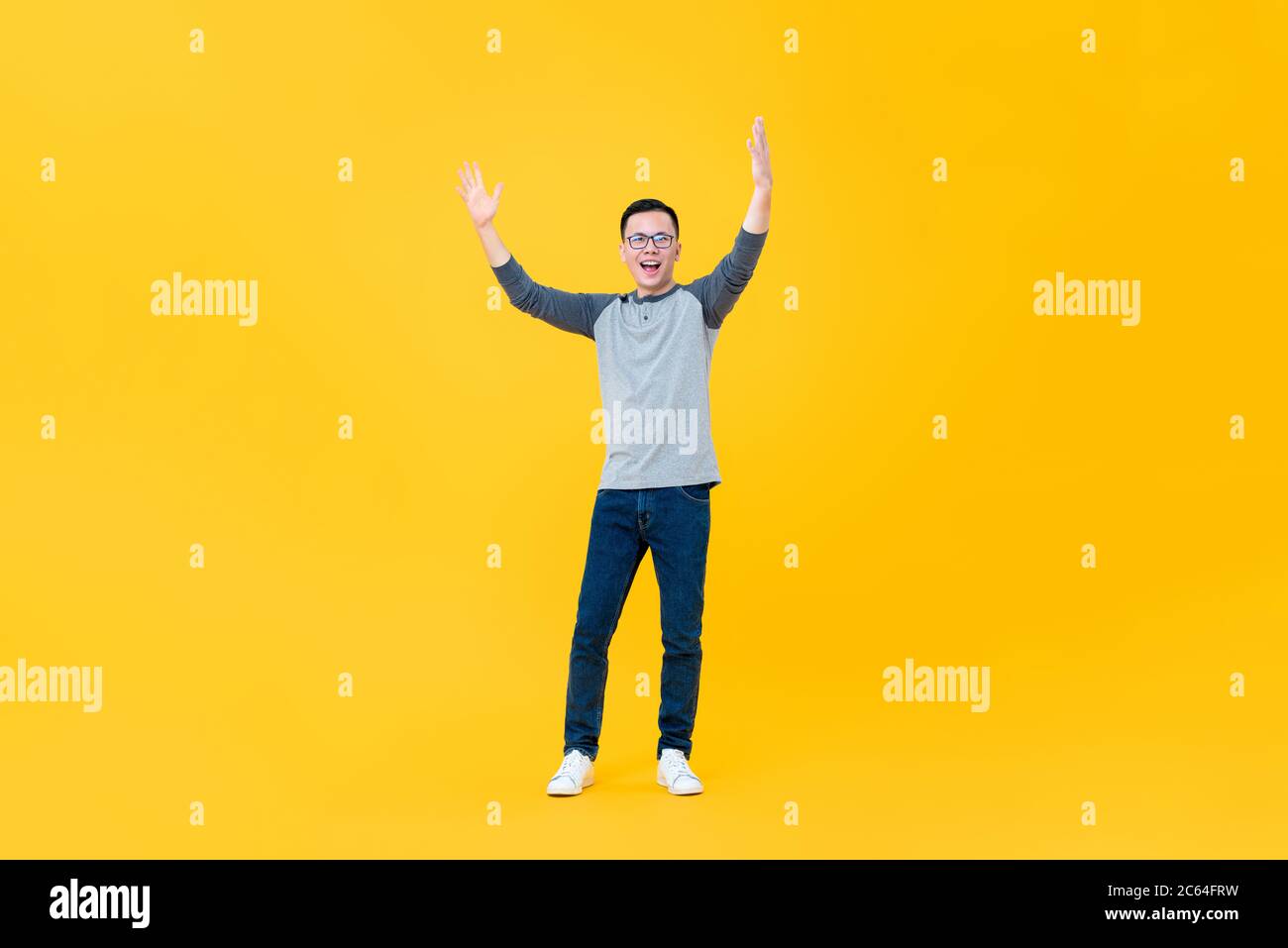 Ritratto a corpo pieno di allegro giovane asiatico che solleva entrambe le braccia in aria isolato su sfondo giallo Foto Stock
