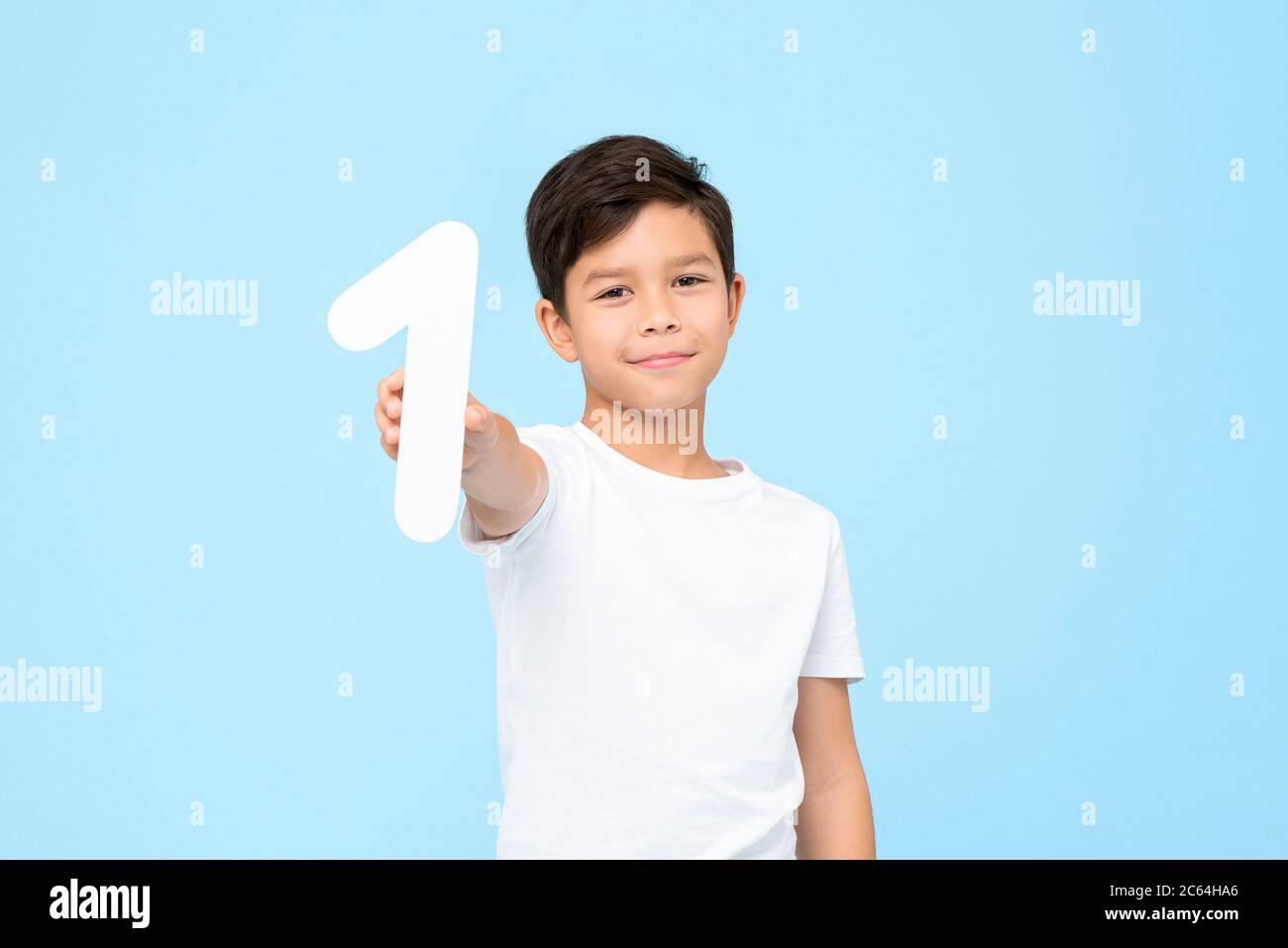 Ritratto di sorridente giovane asiatico che tiene e mostra il taglio numero uno in studio isolato sfondo blu per il concetto di istruzione Foto Stock
