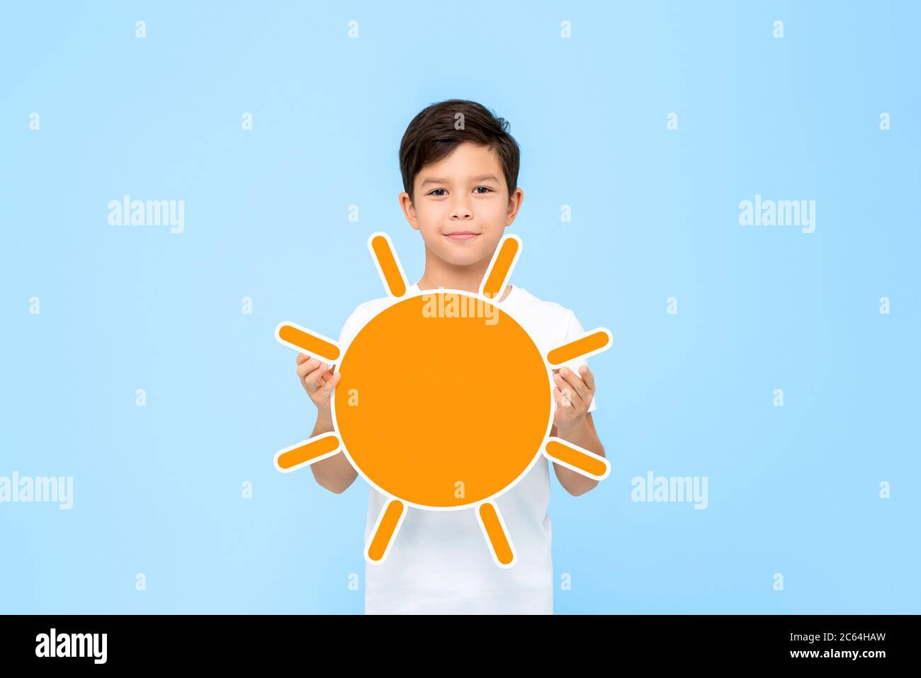 Divertente ritratto di sorridente ragazzo asiatico che tiene orange taglio del sole con entrambe le mani in uno sfondo blu studio isolato Foto Stock