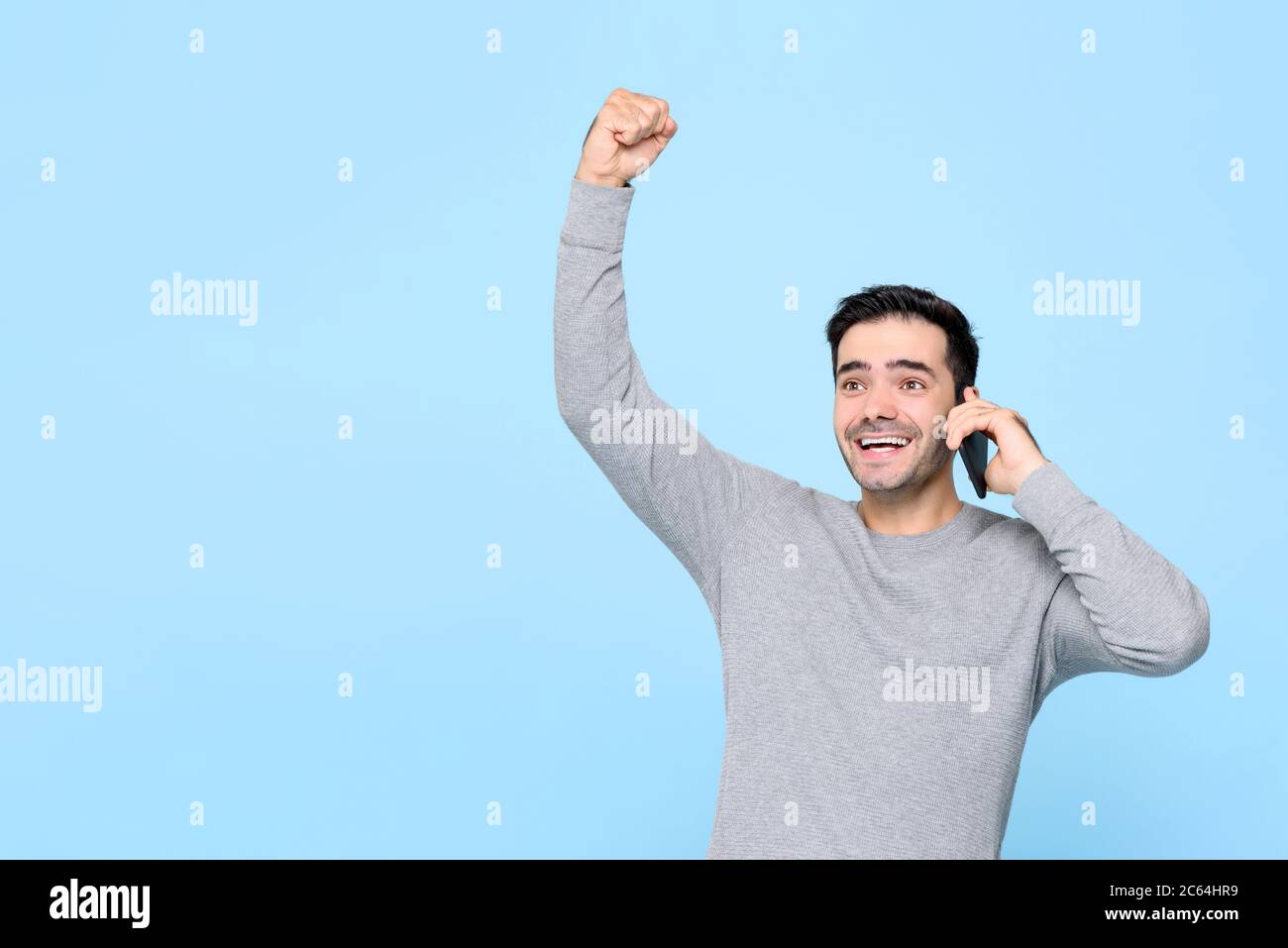 Ritratto di sorridente bel giovane caucasico con pugno sollevato parlare al telefono ascoltando buone notizie in studio isolato sfondo blu Foto Stock