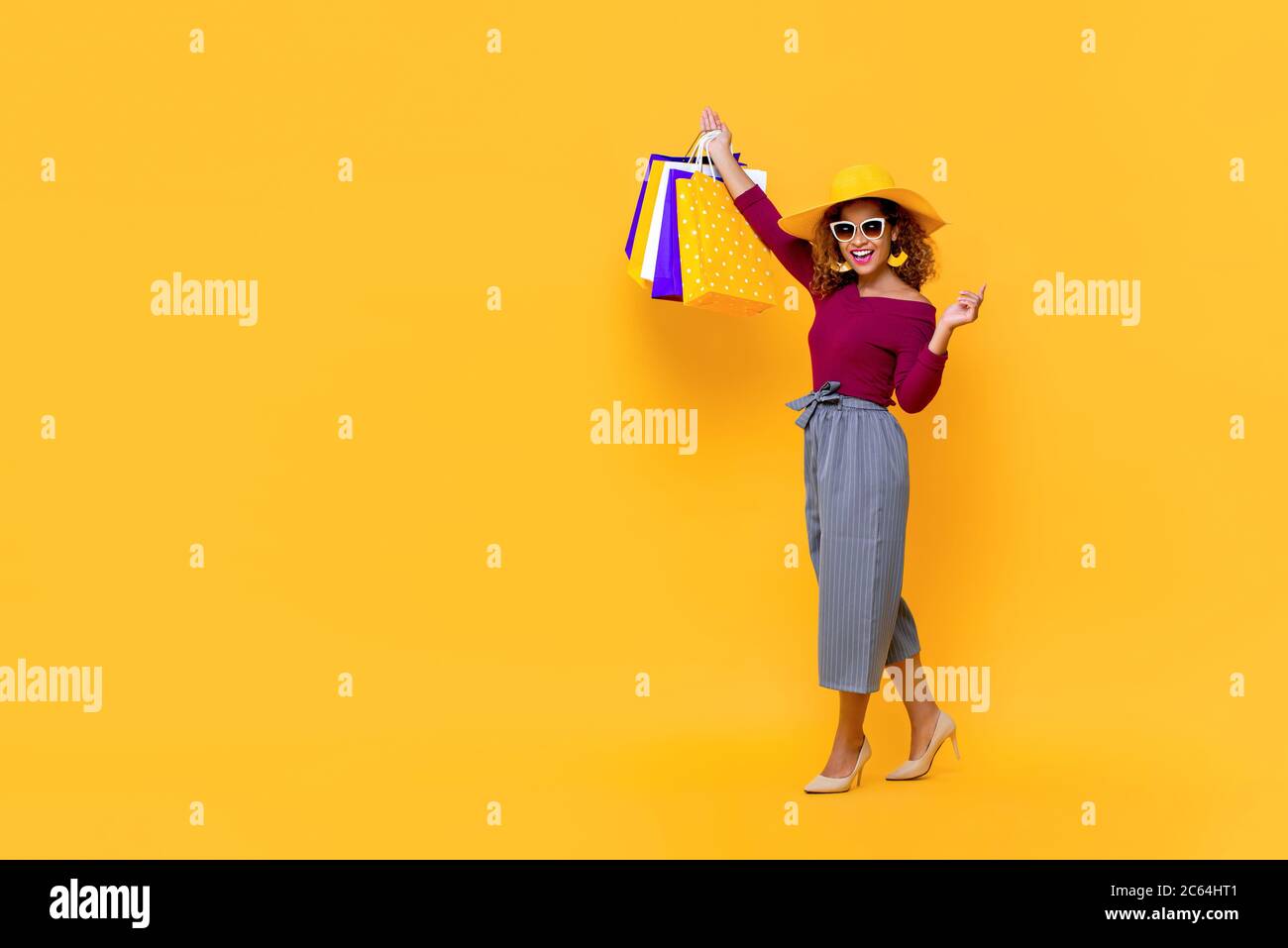 Ritratto di una giovane donna afroamericana sorridente e attraente che solleva le sue borse in uno studio isolato di sfondo giallo Foto Stock