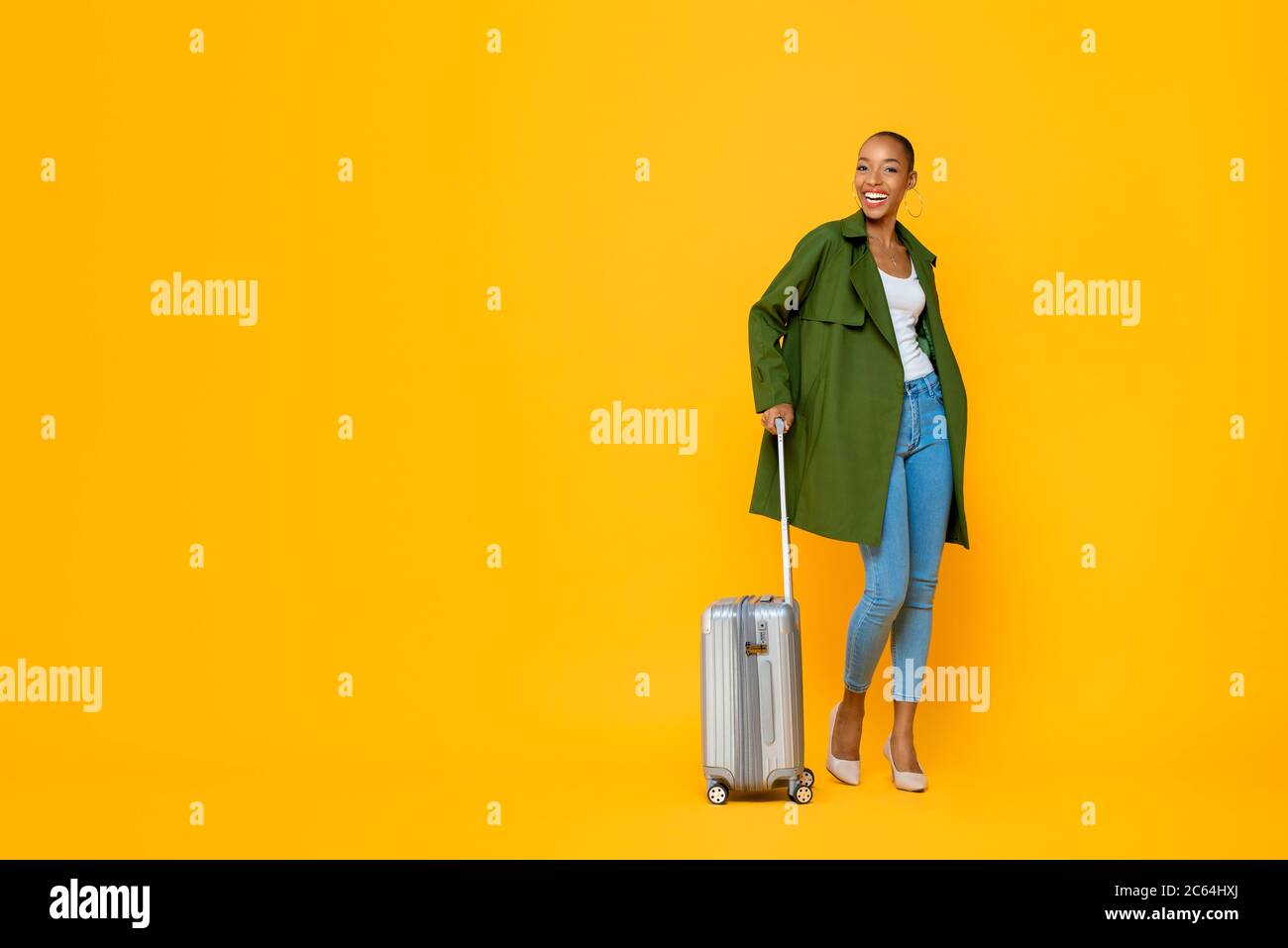Ritratto a lunghezza intera di giovane e felice donna turistica afroamericana in piedi mentre si tiene il bagaglio in uno studio isolato sfondo giallo Foto Stock