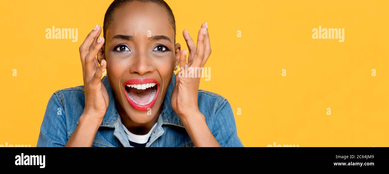 Primo piano panoramico ritratto di giovane donna afro-americana spaventata urlando con entrambe le mani sollevate isolate su sfondo giallo studio Foto Stock