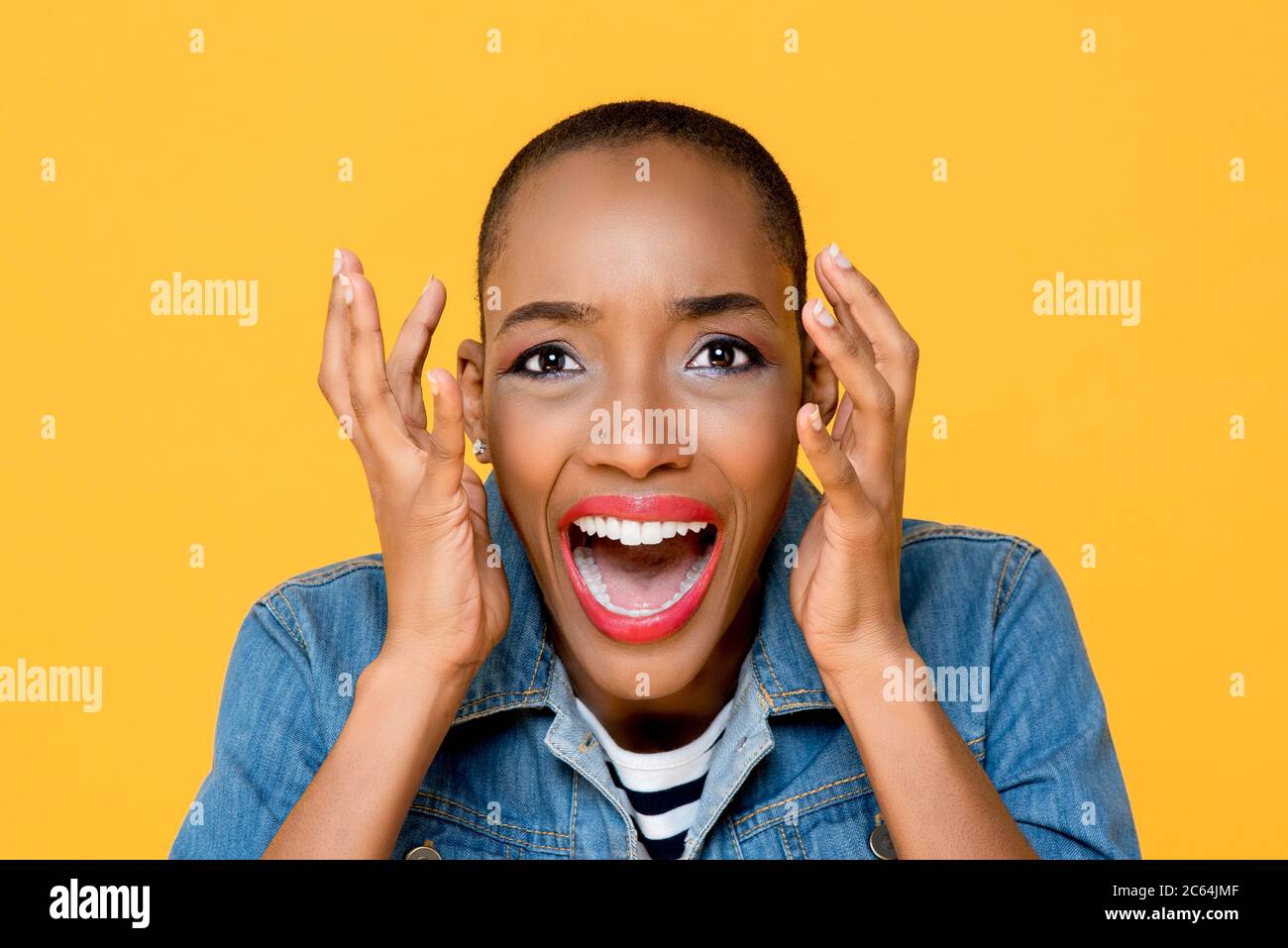 Primo piano ritratto di giovane donna afro-americana spaventata urlando con entrambe le mani sollevate in uno studio isolato sfondo giallo Foto Stock