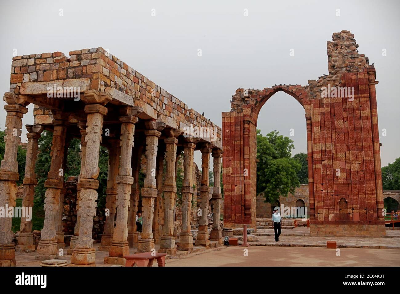 Un ufficiale di sicurezza che cammina sotto le strutture della moschea di Quwwat-al-Islam al Qutb Minar Complex, Mehrauli, Delhi, India. Foto Stock