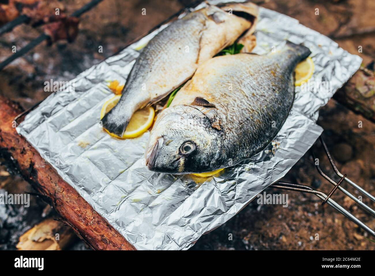 Il pesce Dorado è fritto su un foglio con limoni e prezzemolo su calici caldi da un fuoco - cucina da campeggio Foto Stock