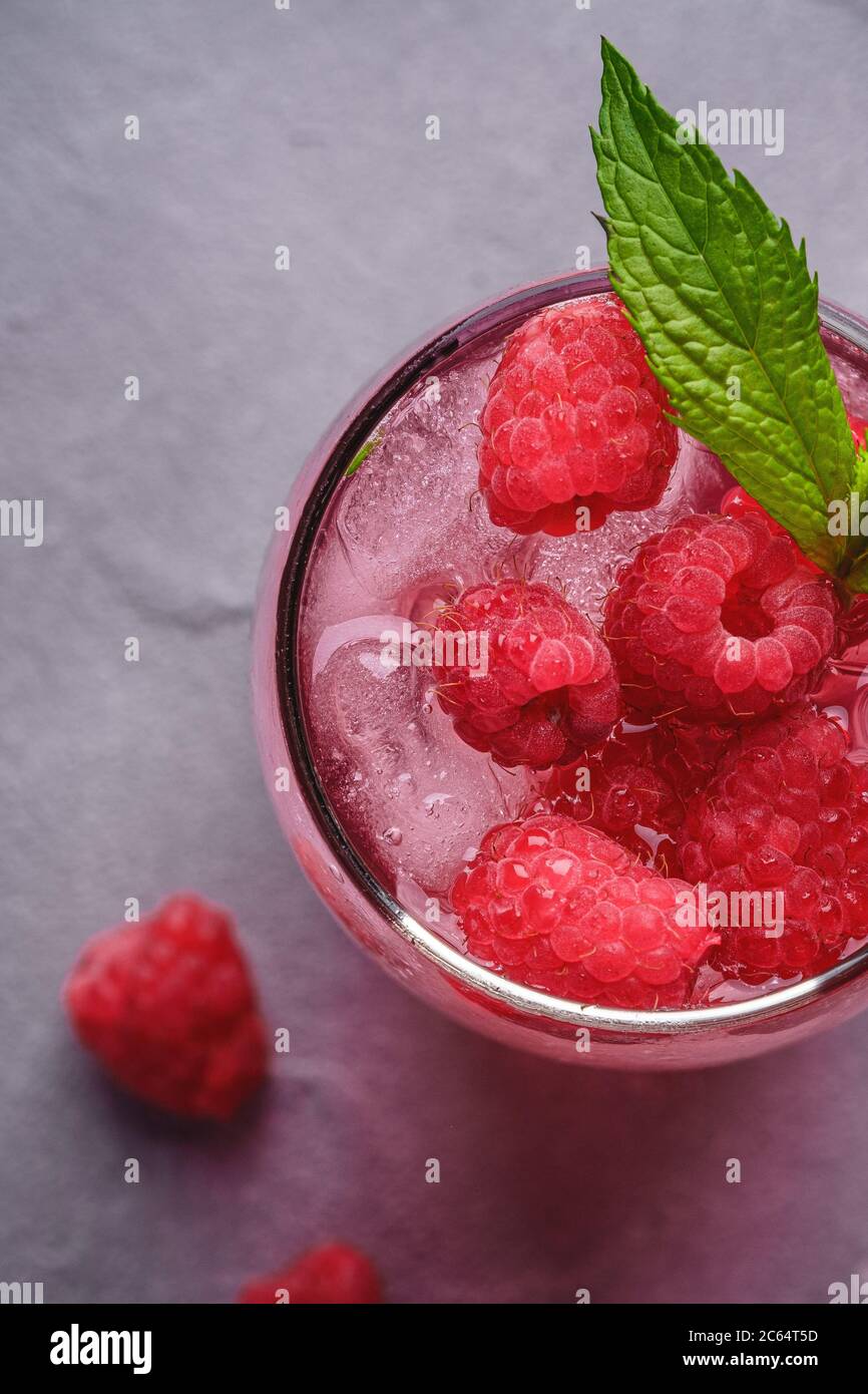 Bevanda fresca di succo di frutti di bosco ghiacciato con menta, limonata estiva di lamponi in vetro su fondo di pietra in cemento, macro vista dall'alto Foto Stock