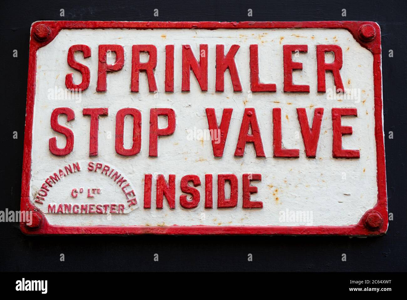 Un vecchio cartello in ghisa rossa e bianca con la valvola di arresto sprinkler all'interno di Hoffmann sprinkler Company Limited di Manchester, Inghilterra, Regno Unito Foto Stock