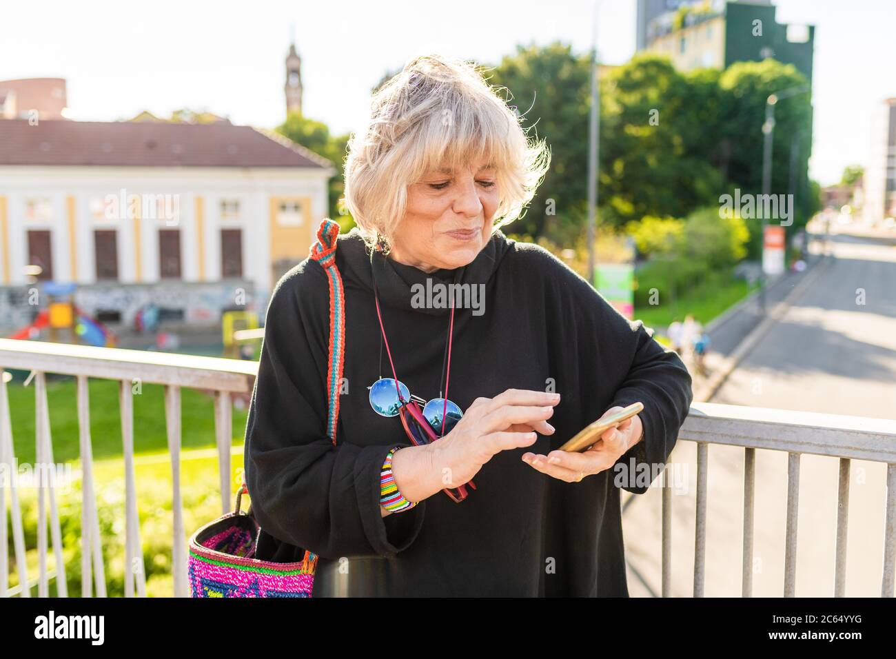 Donna anziana con capelli biondi in piedi sul ponte, utilizzando il telefono cellulare. Foto Stock