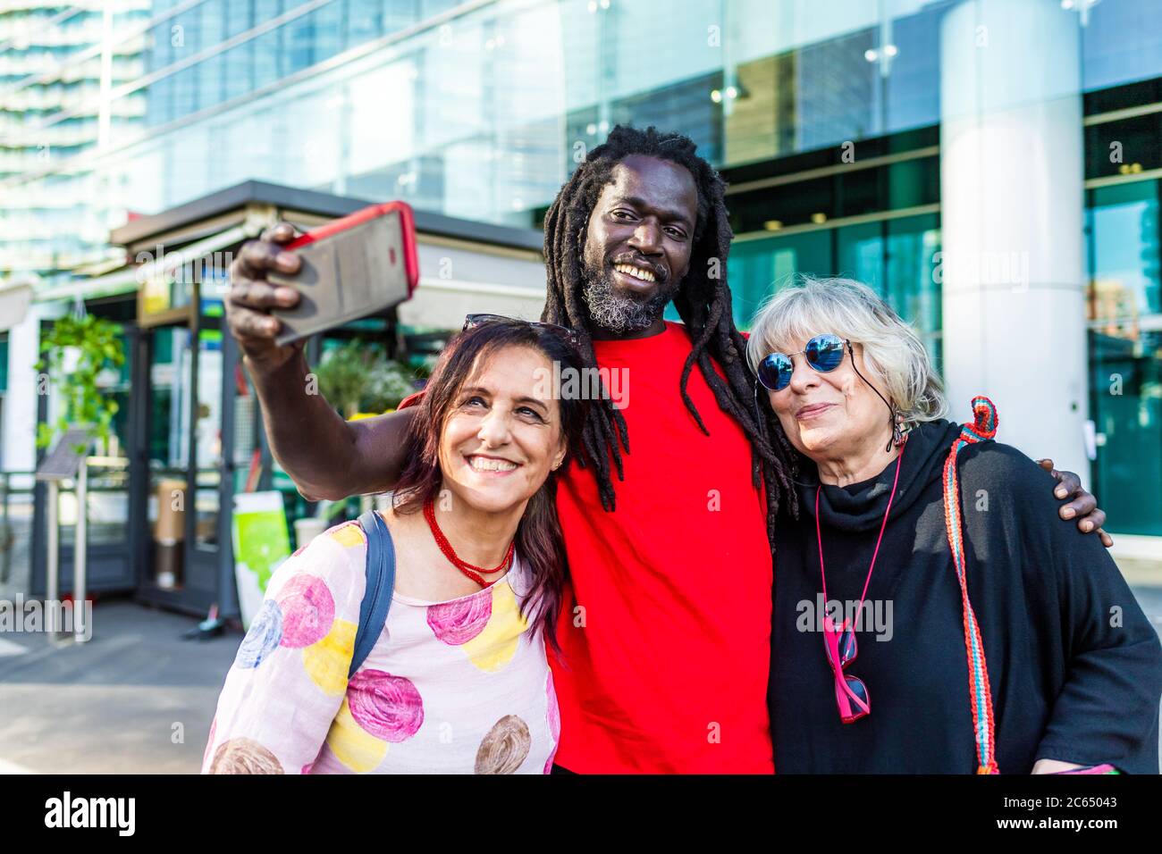 Uomo nero con dreadlock e due donne caucasiche che prendono selfie con il telefono cellulare. Foto Stock
