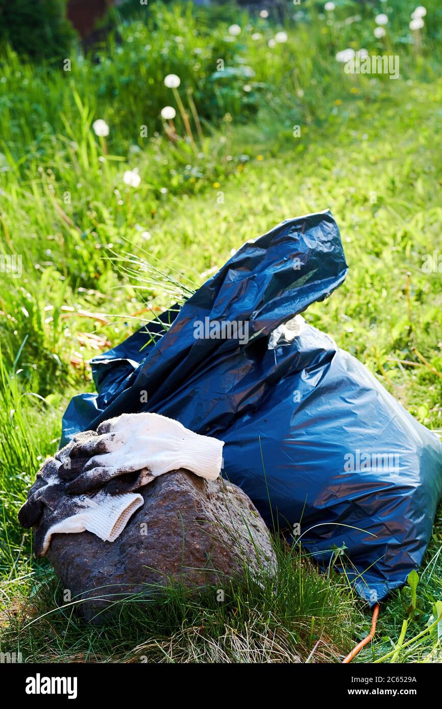 Pulizia della natura e dell'ambiente, un sacchetto per rifiuti pieno di rifiuti e guanti da lavoro. Simbolo di tutela ambientale e della tutela del pianeta Terra Foto Stock