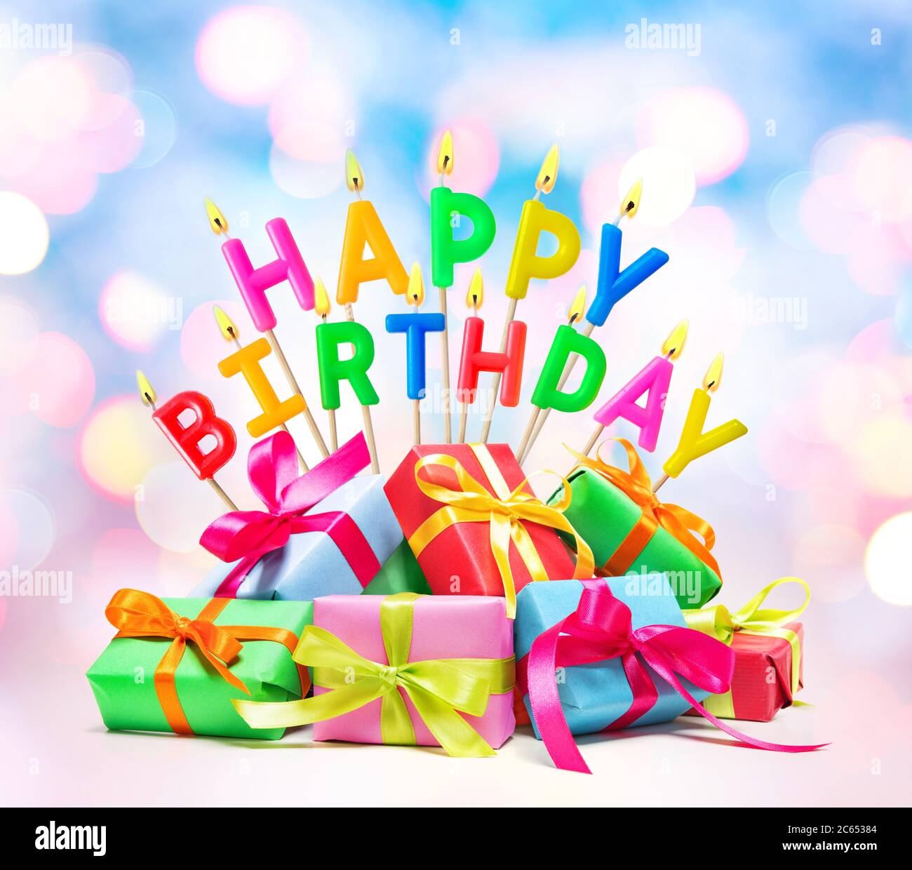 Bruciando candele di compleanno felici con scatole di regalo su sfondo colorato Foto Stock