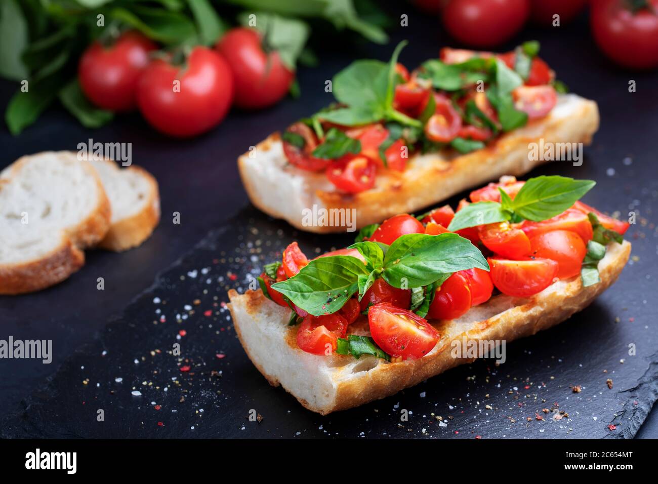 Bruschetta fatta in casa con pomodori ciliegini e salsa al basilico su una tavola di ardesia. Cucina italiana. Antipasti. Cibo vegano Foto Stock