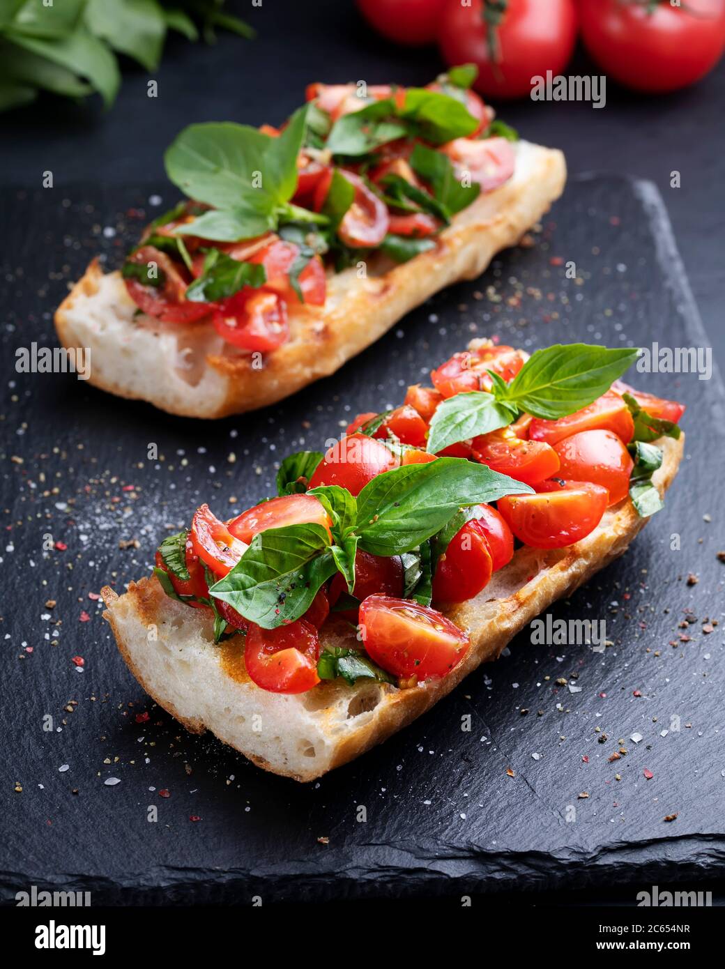 Bruschetta fatta in casa con pomodori ciliegini e salsa al basilico su una tavola di ardesia. Cucina italiana. Antipasti. Cibo vegano Foto Stock