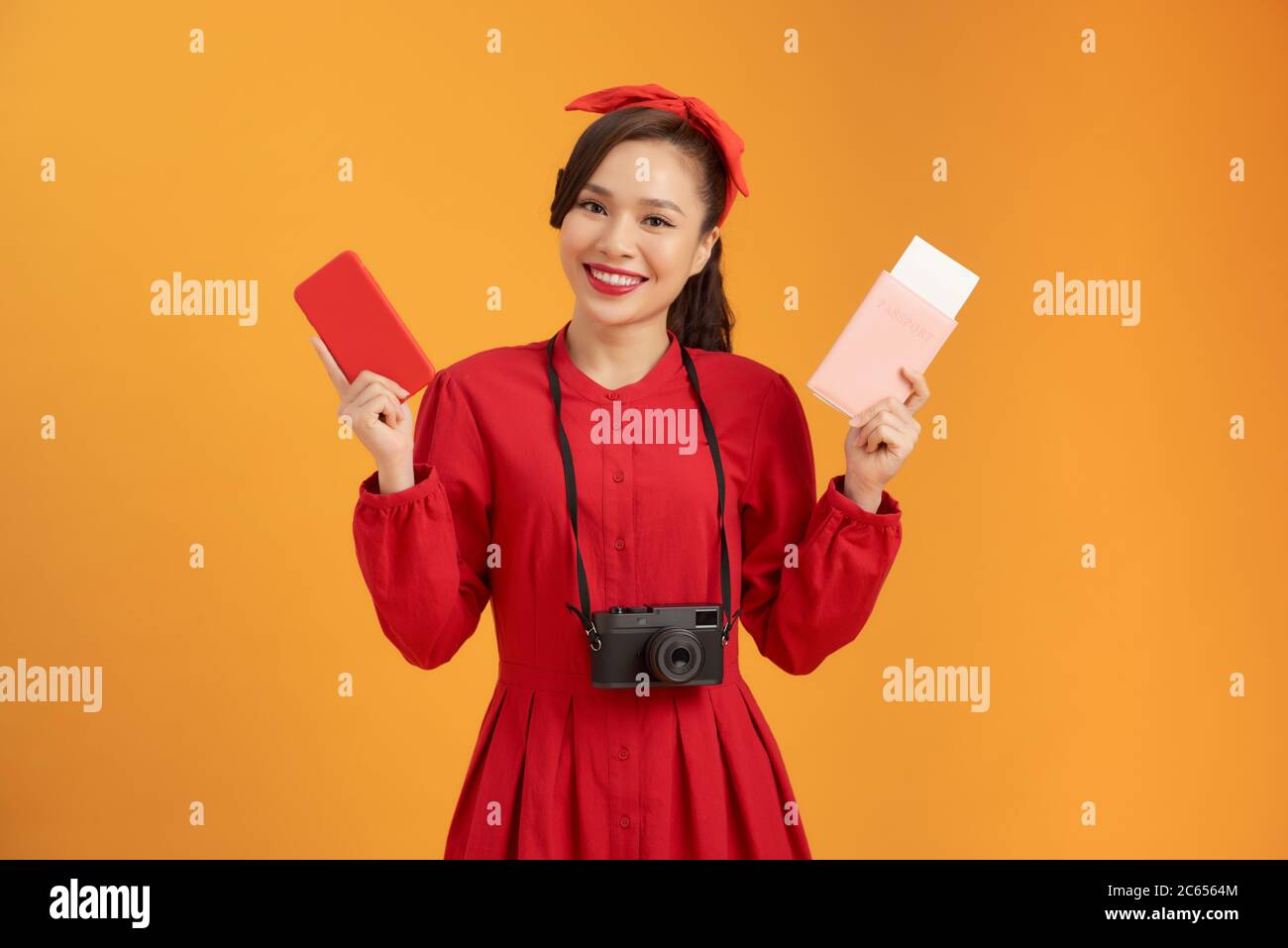 Felice turista donna in estate vestito rosso tenendo passaporto isolato su sfondo arancione. Foto Stock