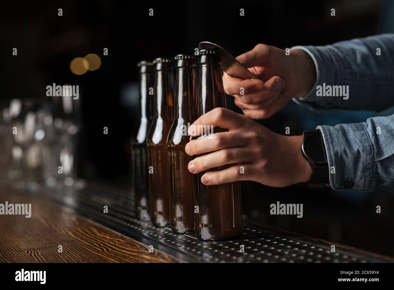 Festa della birra. La camicia barista apre le bottiglie di birra sul bancone del bar su sfondo sfocato Foto Stock