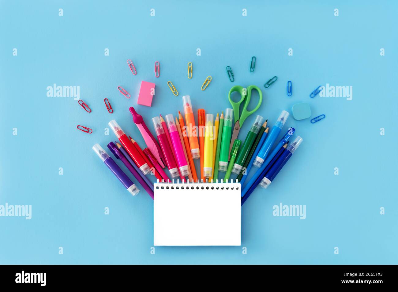 Ritorno a scuola con blocco note aperto e varietà di forniture scolastiche in colori arcobaleno su sfondo blu pastello. Disposizione piatta. Primo piano. Spazio di copia. Foto Stock