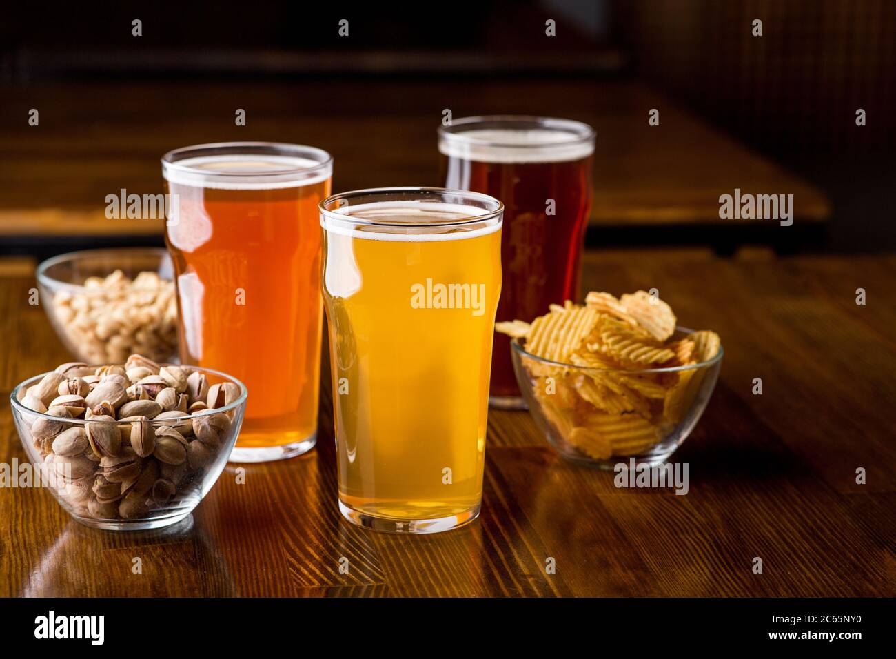 Bevande diverse nei bicchieri. Pistacchi, patatine, arachidi in vetro in lastre su tavola di legno Foto Stock