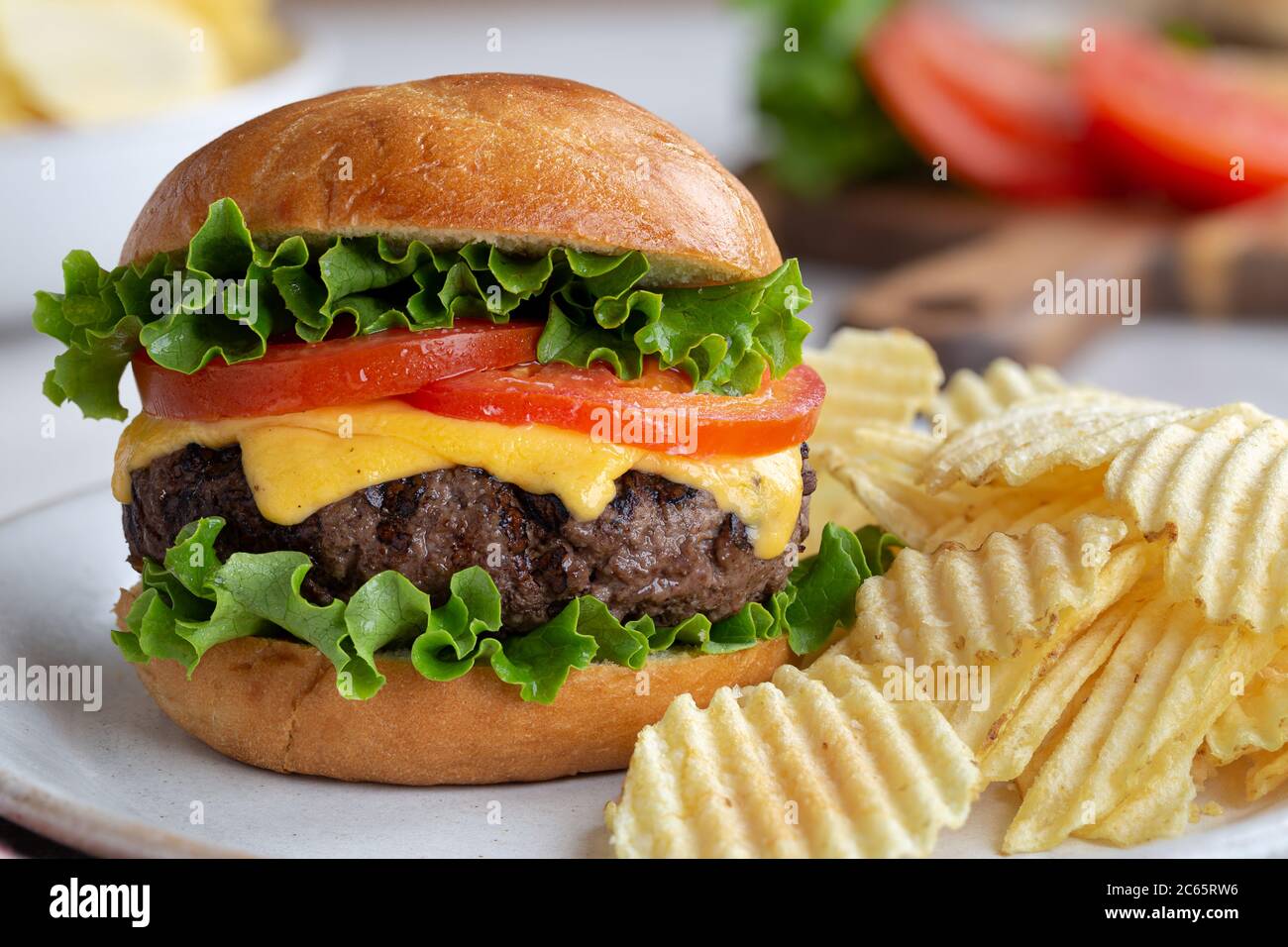 Succosa cheeseburger alla griglia con lattuga e patatine e pomodoro su un piatto Foto Stock