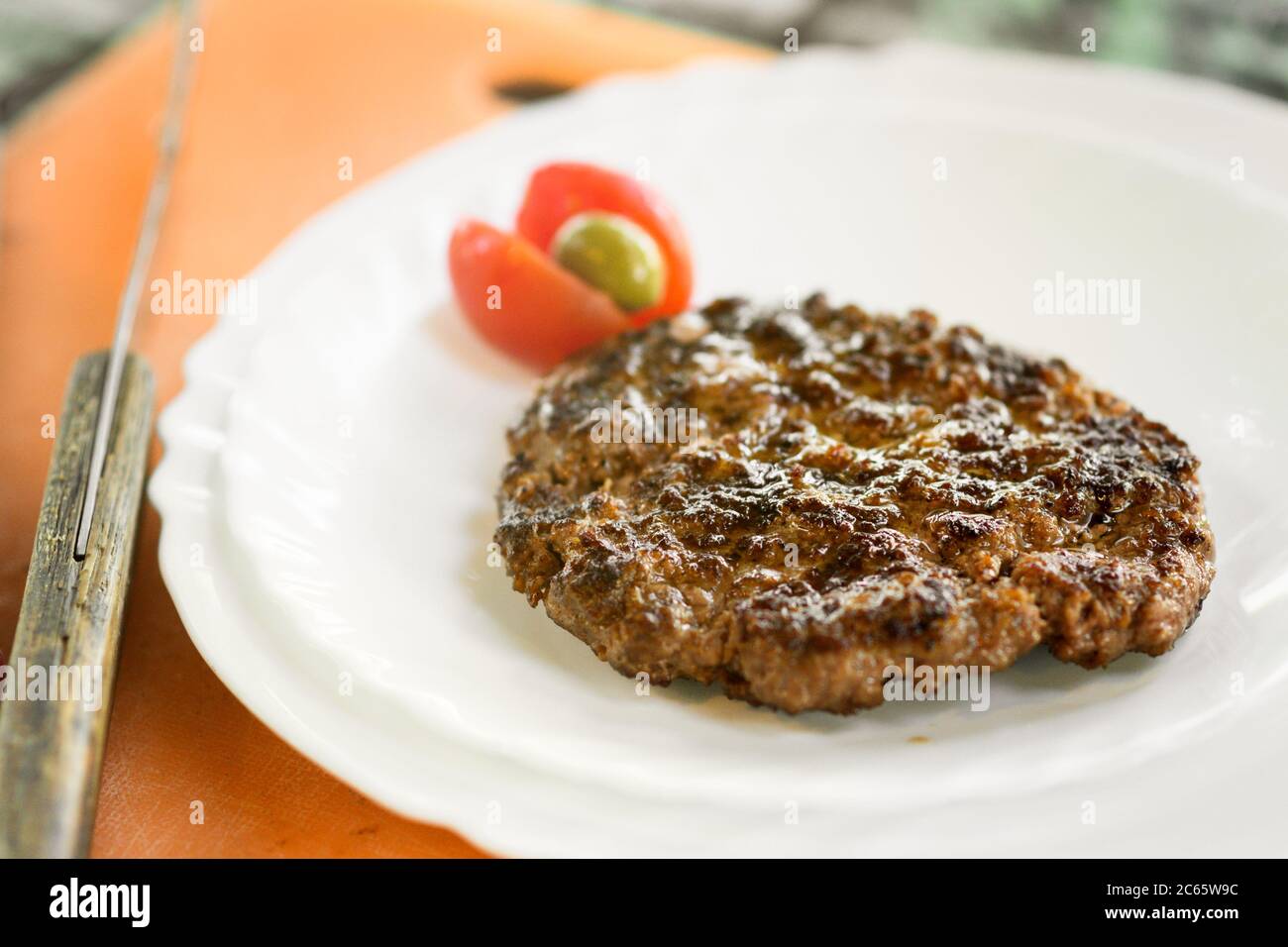 Polpettine di hamburger di manzo cotto su un piatto servito con pomodoro fresco e olive in primo piano con un coltello a fianco Foto Stock