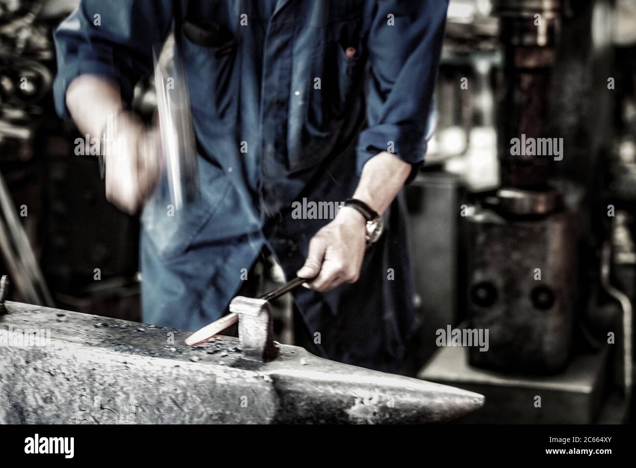 Fabbro che lavora un ferro incandescente in una vecchia fucina Foto Stock