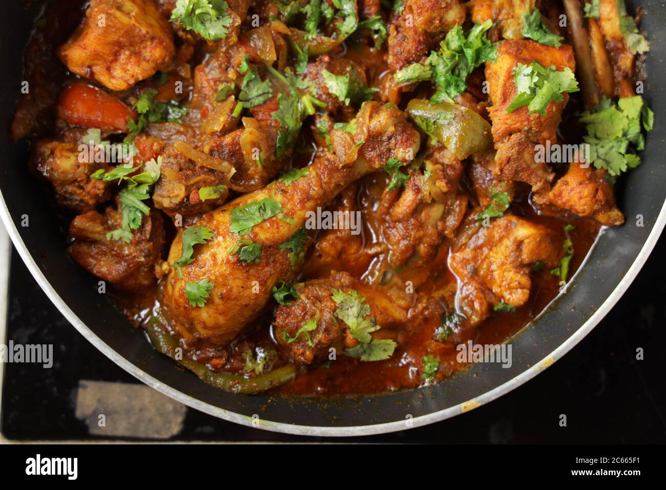 Pollo curry Chicken masala, indiano piccante pollo curry guarnito con foglie di coriandolo e disposto in una padella di cottura nero colorato, fuoco selettivo Foto Stock