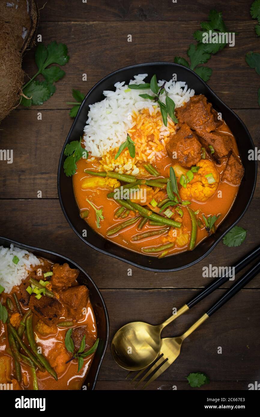 Curry rosso thai vegano con seitan, fagioli e cavolfiore su riso, servito in ciotole nere Foto Stock