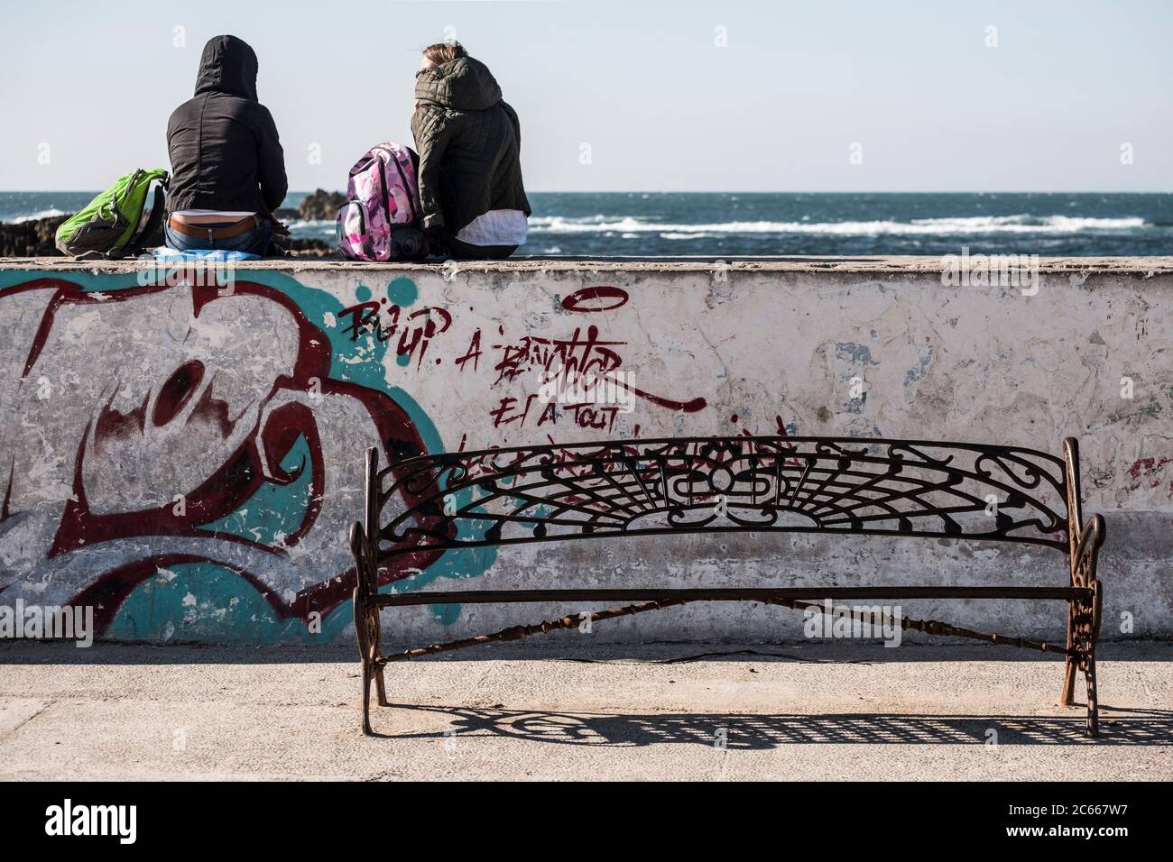 Due persone sedute su un muro di banchina a Essaouira che si affaccia sull'Oceano Atlantico Foto Stock