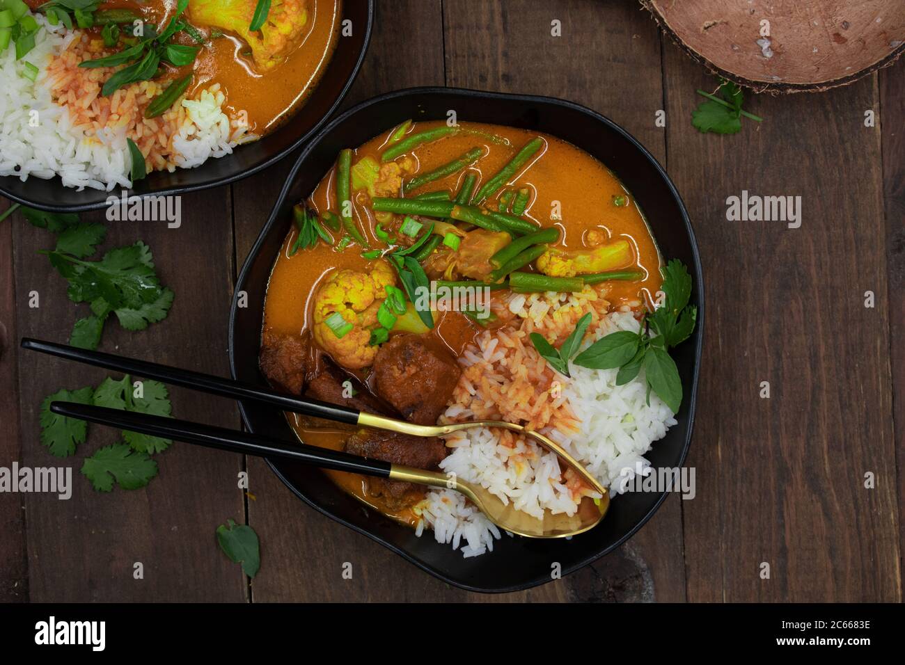 Curry rosso thai vegano con seitan, fagioli e cavolfiore su riso, servito in ciotole nere Foto Stock
