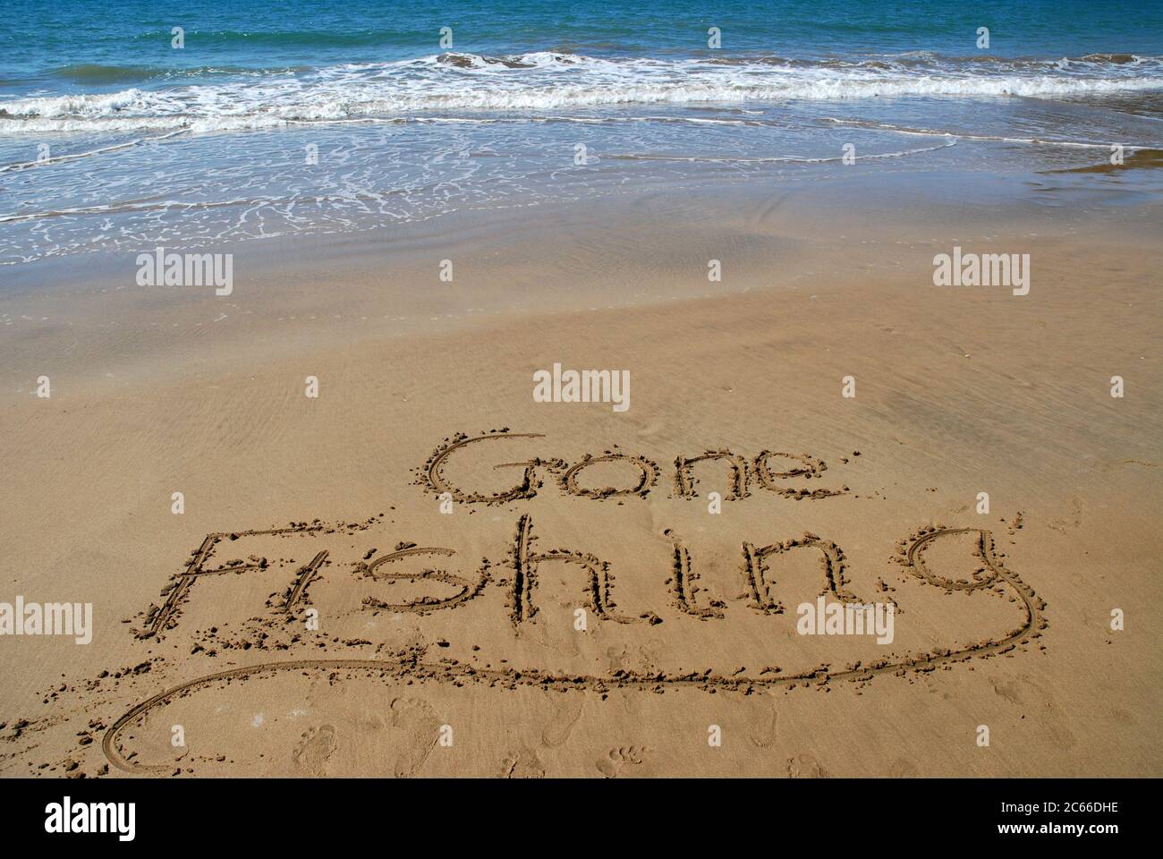 Pesca andata scritta in sabbia sulla spiaggia con surf e mare blu oltre. Foto Stock