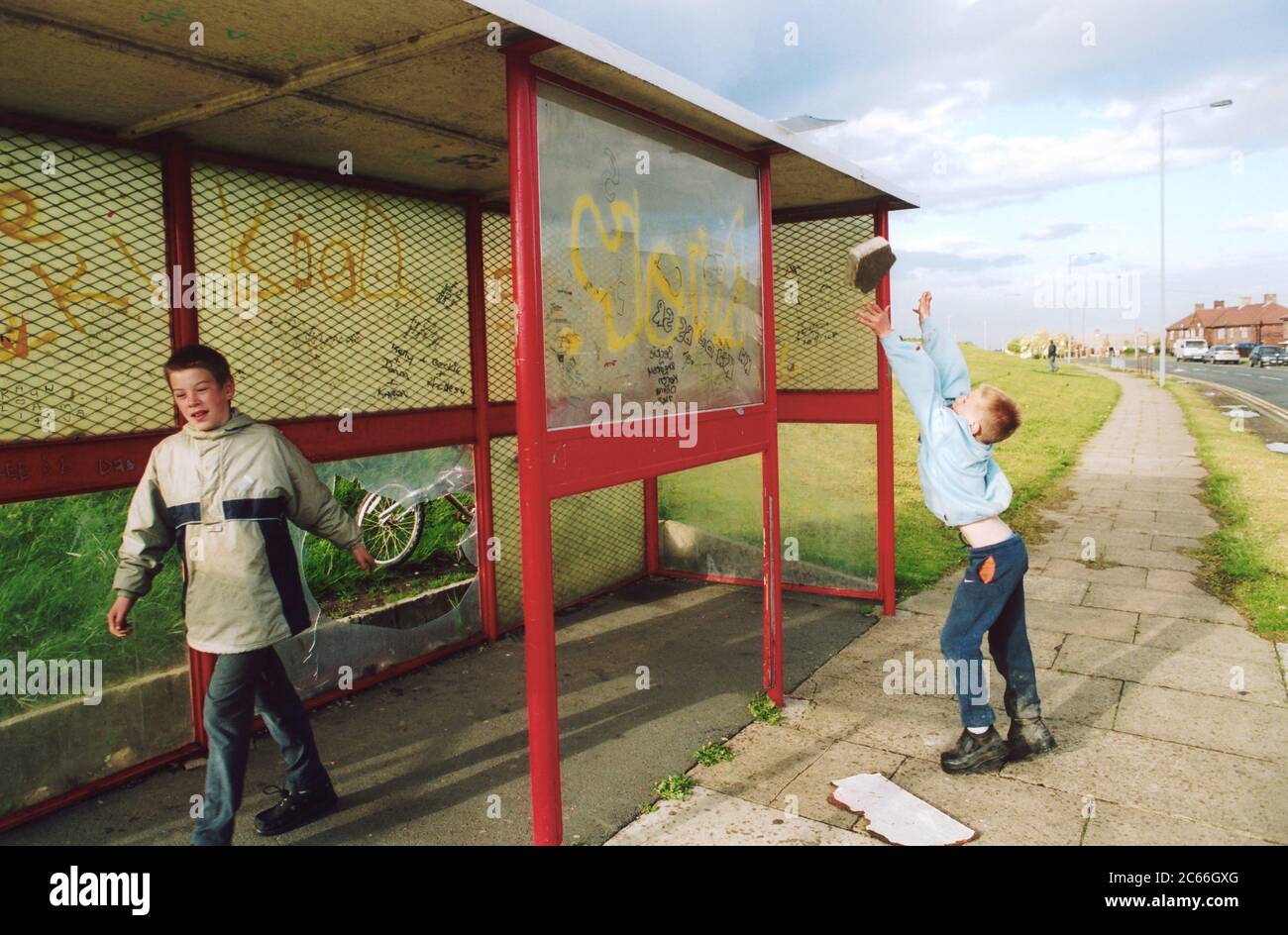 Ragazzi che giocano in un rifugio per autobus; Bradford council estate; Regno Unito, Boy che getta grumi di cemento Foto Stock
