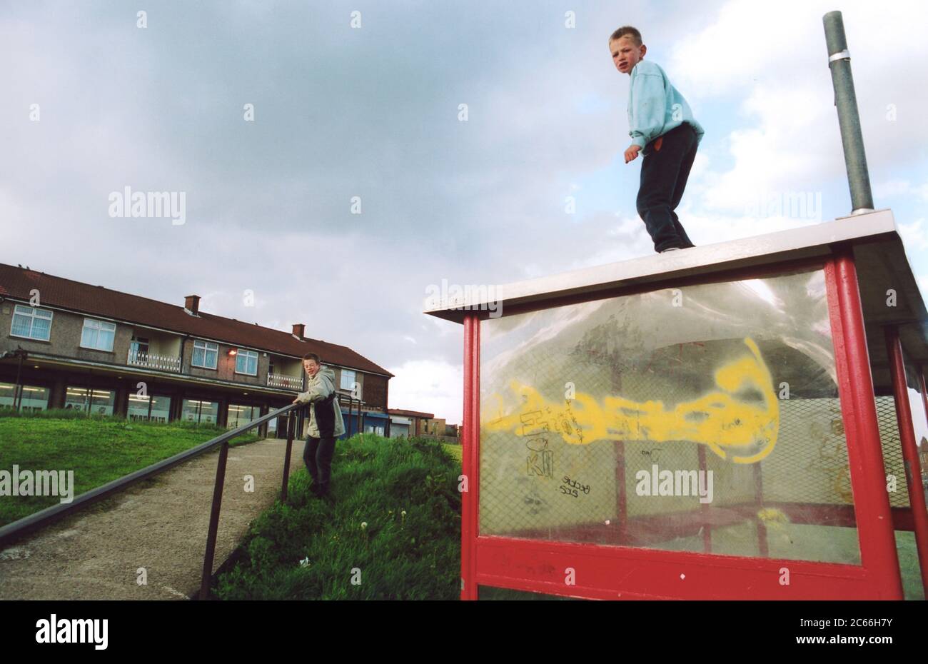 Ragazzi che giocano sul rifugio degli autobus in run down council estate; Bradford UK Foto Stock