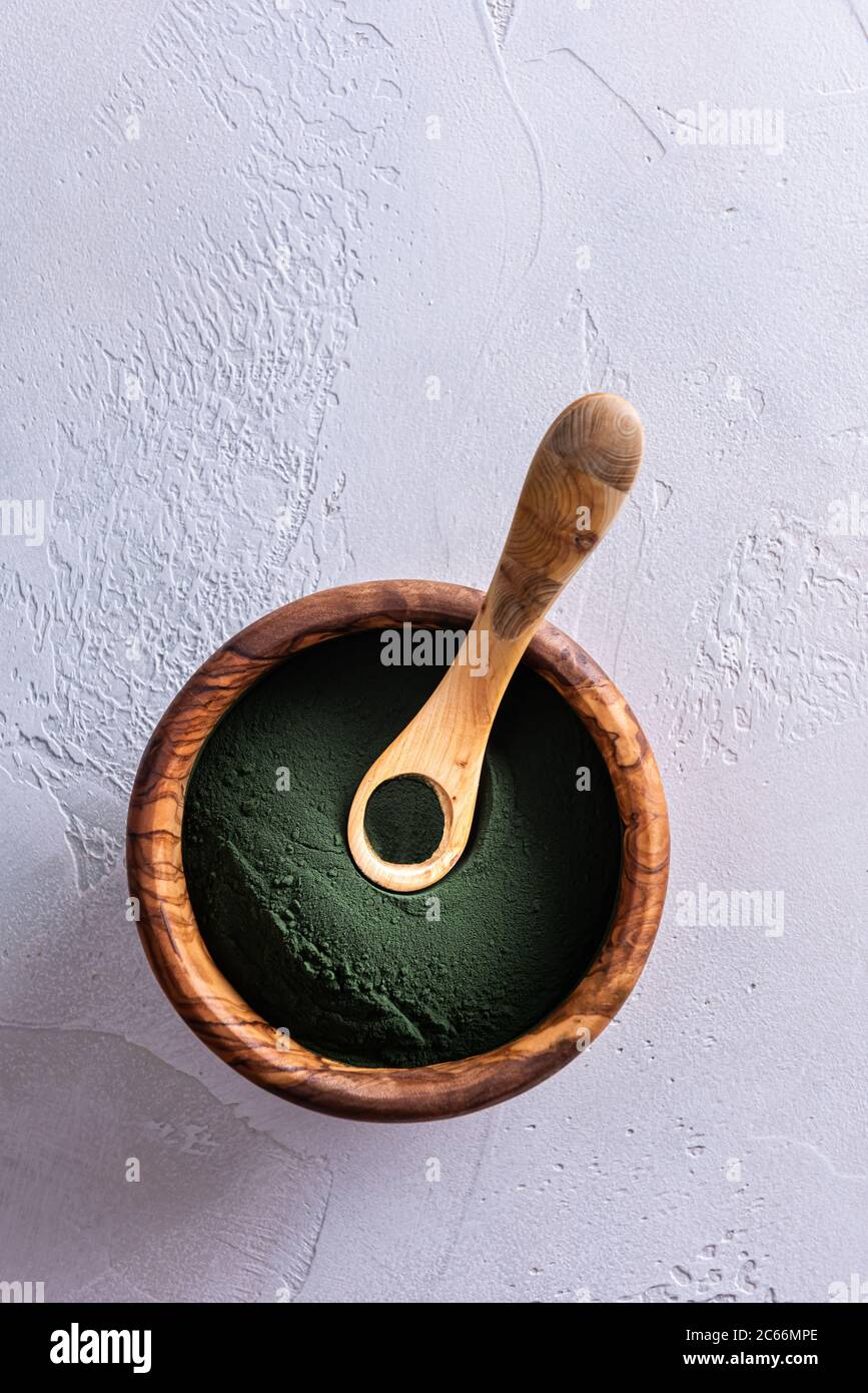 Polvere di clorella verde o spirulina in ciotola marrone di legno naturale dall'alto e un piccolo cucchiaio pieno sopra di esso. Cibo sano superfood mangiare e mangiare co Foto Stock