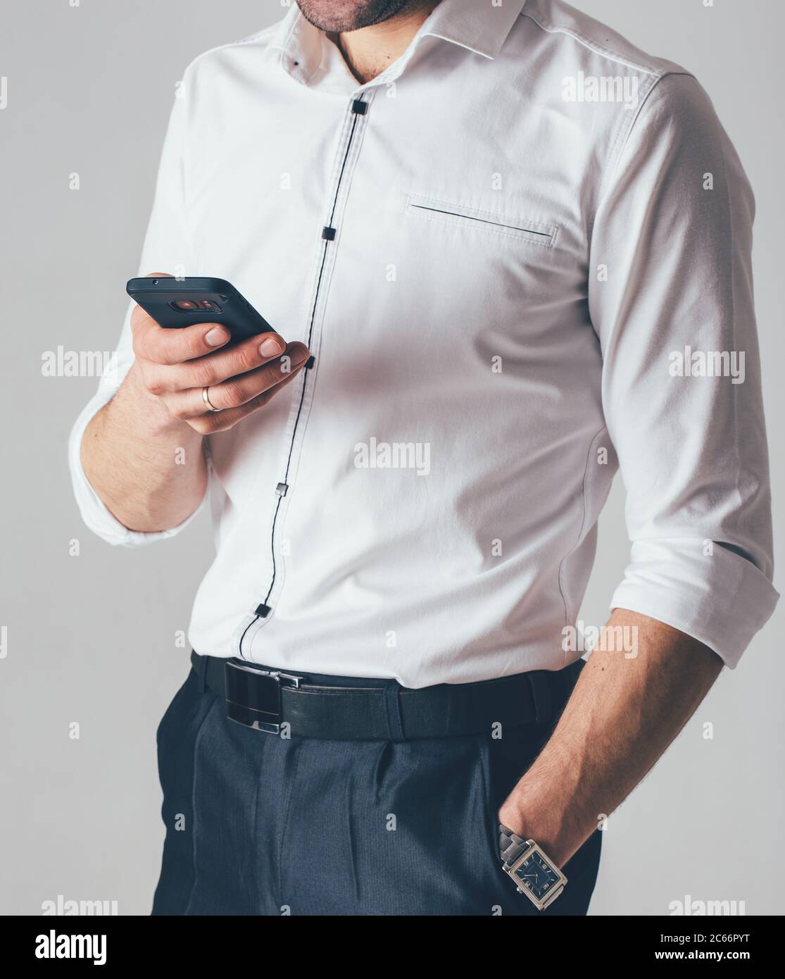 un uomo d'affari in una camicia bianca e pantaloni neri tiene un telefono  in mano in ufficio. Un uomo indossa un orologio da polso nella mano  sinistra Foto stock - Alamy