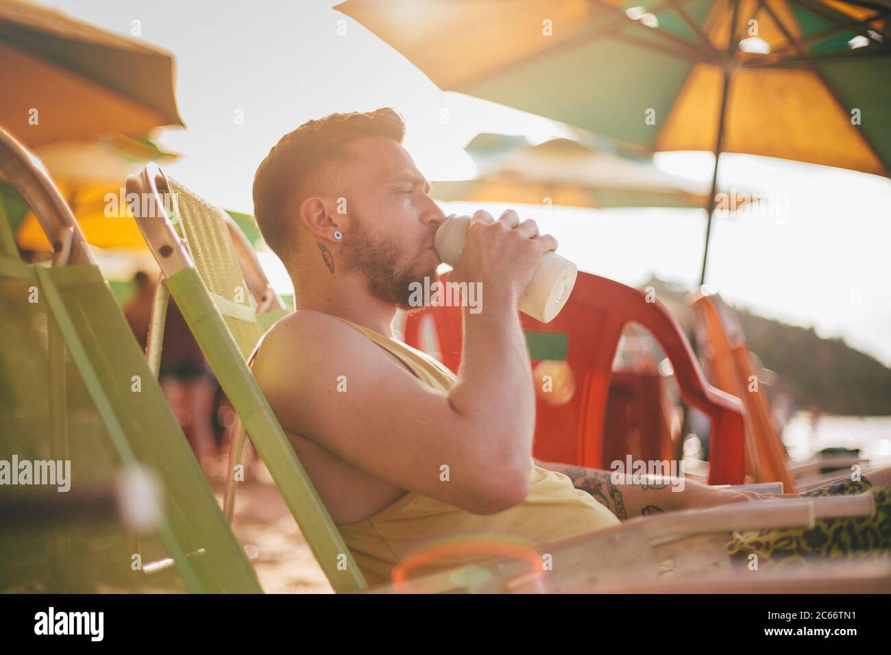 un giovane biondo che beve una birra sulla spiaggia Foto Stock