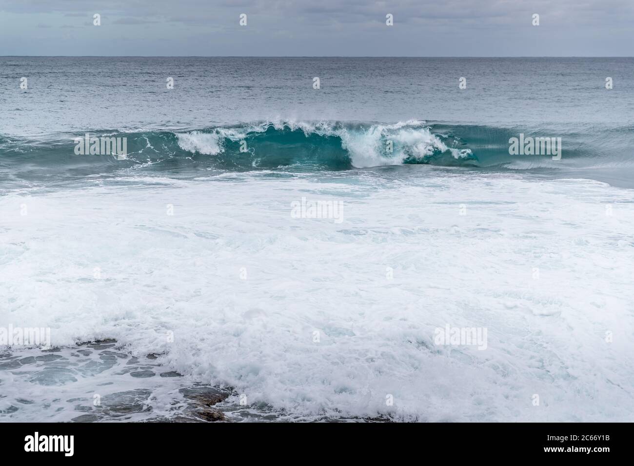 Onde che si infrangono in una riva rocciosa piena di grandi rocce e che rompono l'acqua che salgono ai lati con un paio di barche ormeggiate all'orizzonte in mare Foto Stock