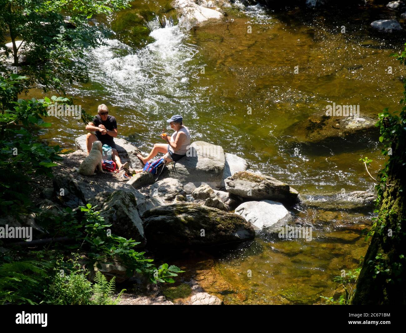La coppia di età media si sedette sulle rocce accanto al fiume East Lyn facendo un picnic, Devon, Regno Unito Foto Stock