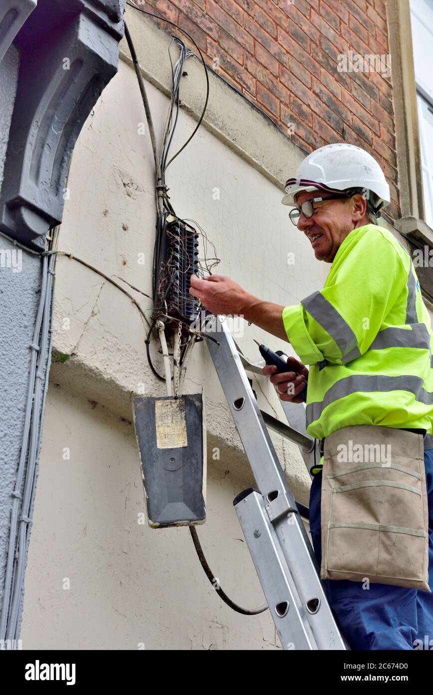 Tecnico telefonico su scala con generatore di toni che testa un nido di fili di rame per tracciare un collegamento nella scatola di derivazione dell'abitazione Foto Stock