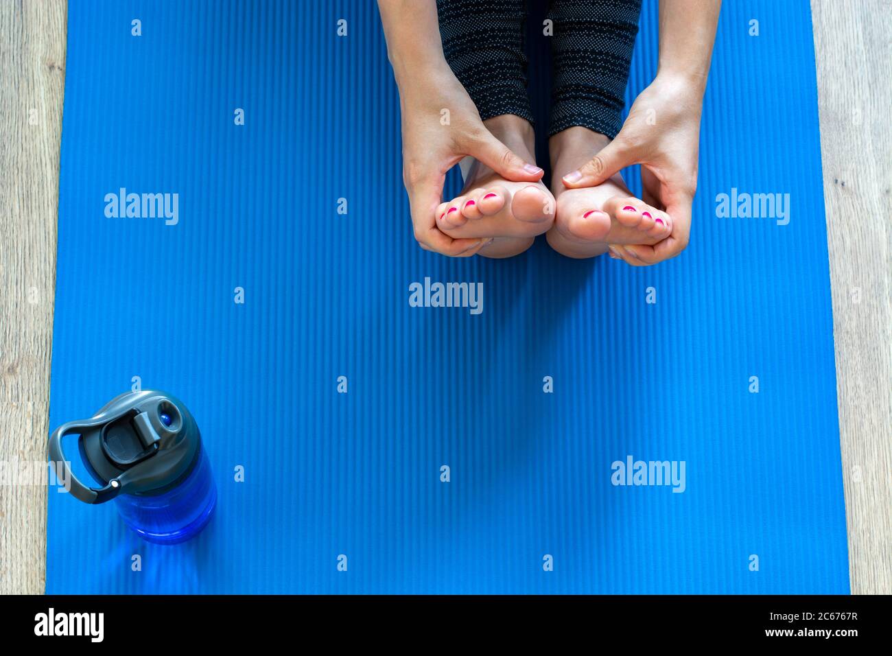 Donna che pratica yoga, facendo esercizio paschimottanasana, seduta piega  posa. Piedi con pedicure rosa di donna e bottiglia d'acqua su tappetino blu  Foto stock - Alamy