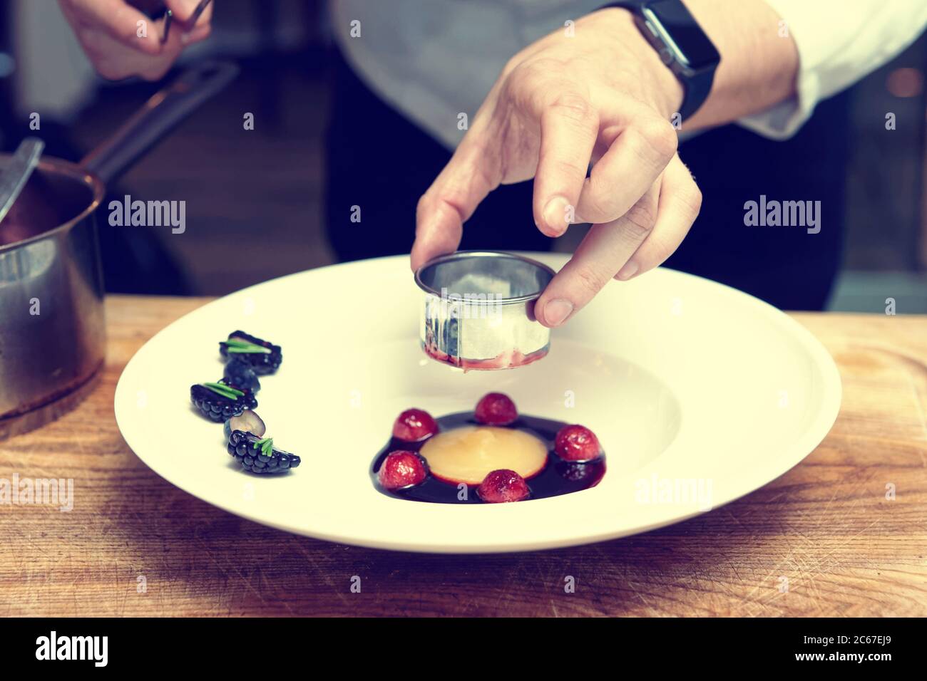 Lo chef professionista sta cucinando piatti gourmet utilizzando un anello culinario in metallo, tonato Foto Stock