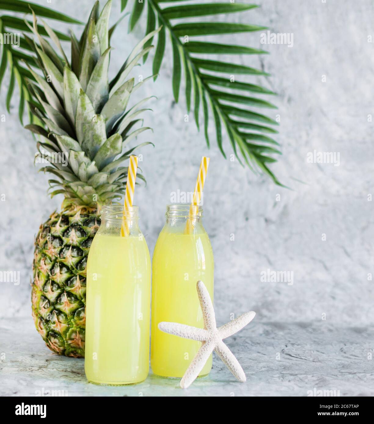 Succo di ananas in bottiglie di vetro con cannucce e frutta all'ananas su fondo di marmo blu. Cocktail estivo. Orientamento verticale. Foto Stock