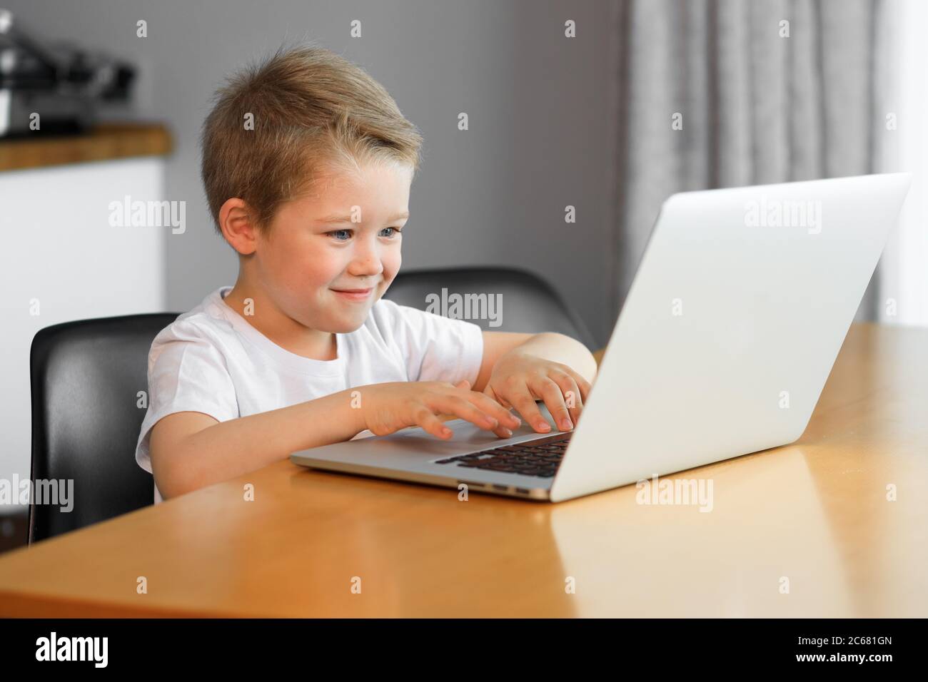 Ragazzo divertente che usa un computer portatile seduto sopra un tavolo a casa Foto Stock