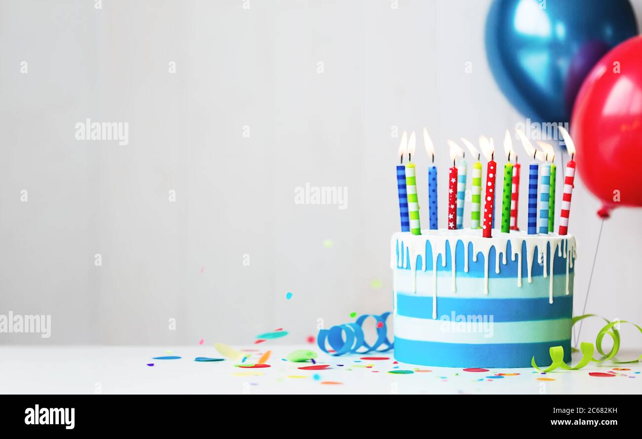 Torta di compleanno con crema di farfalle a righe colorate con candele di compleanno e palloncini Foto Stock